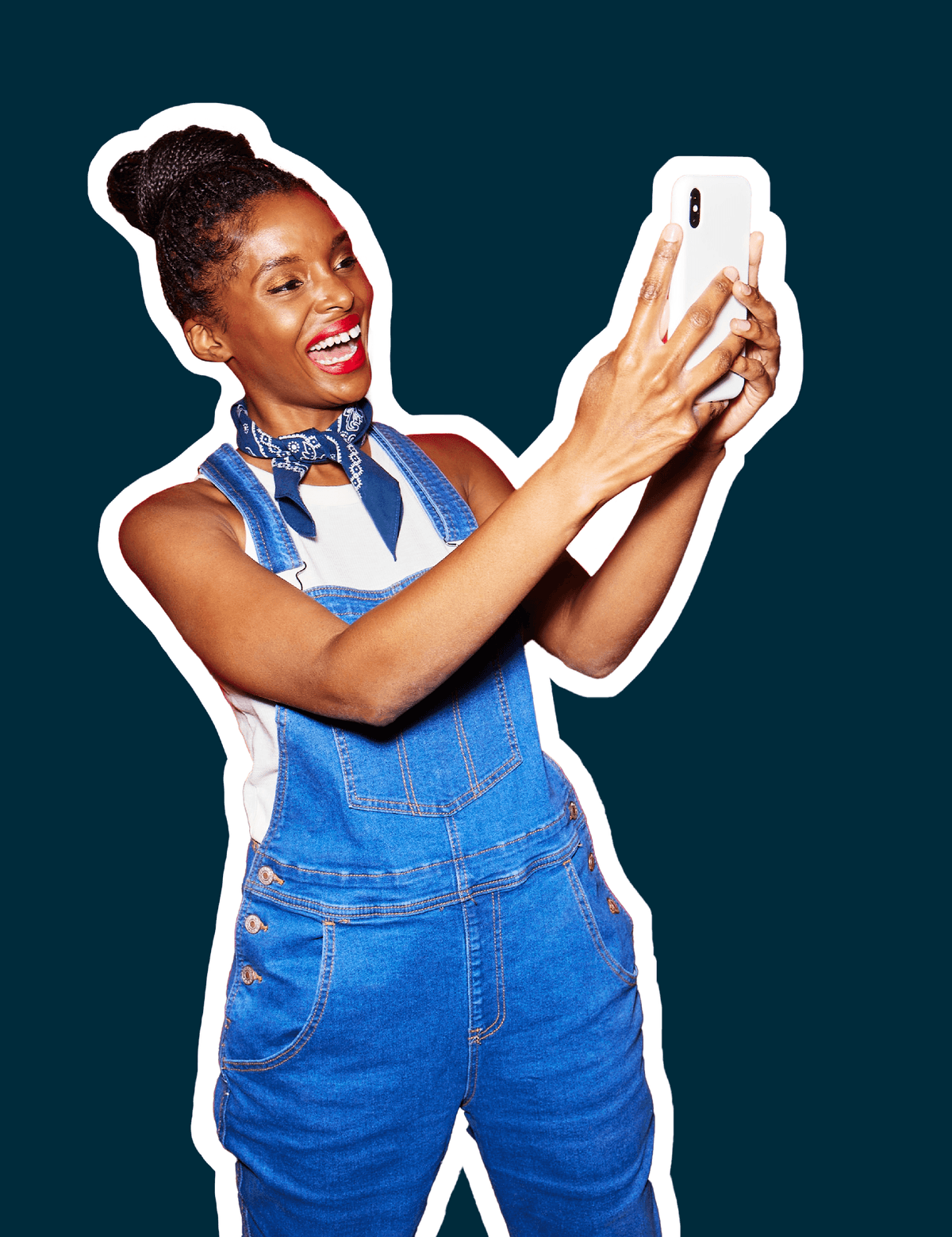 Woman standing and smiling taking a selfie while wearing overalls